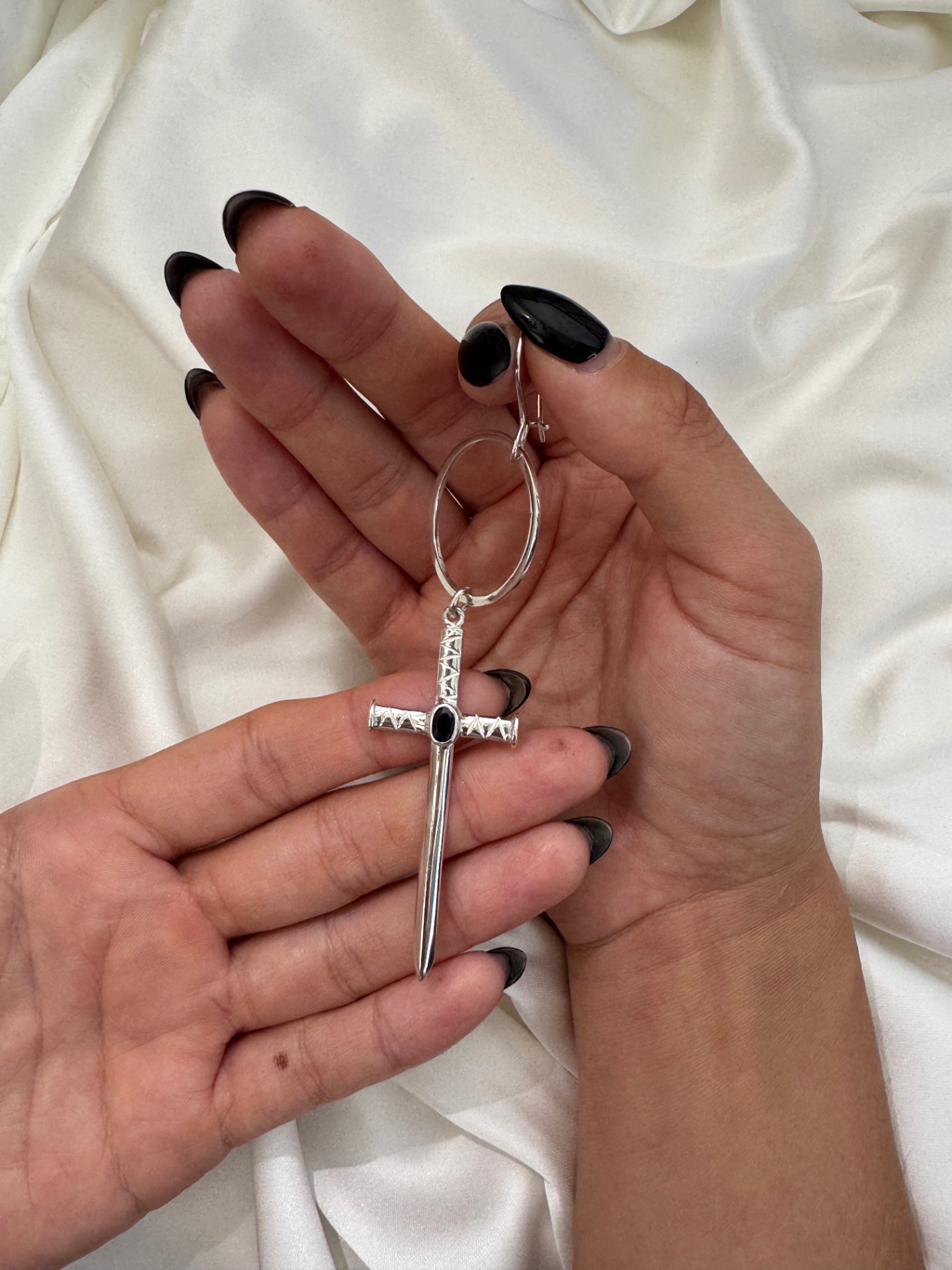 The Sapphire Cross, handcrafted 999 silver set with a natural sapphire, held against ivory silk