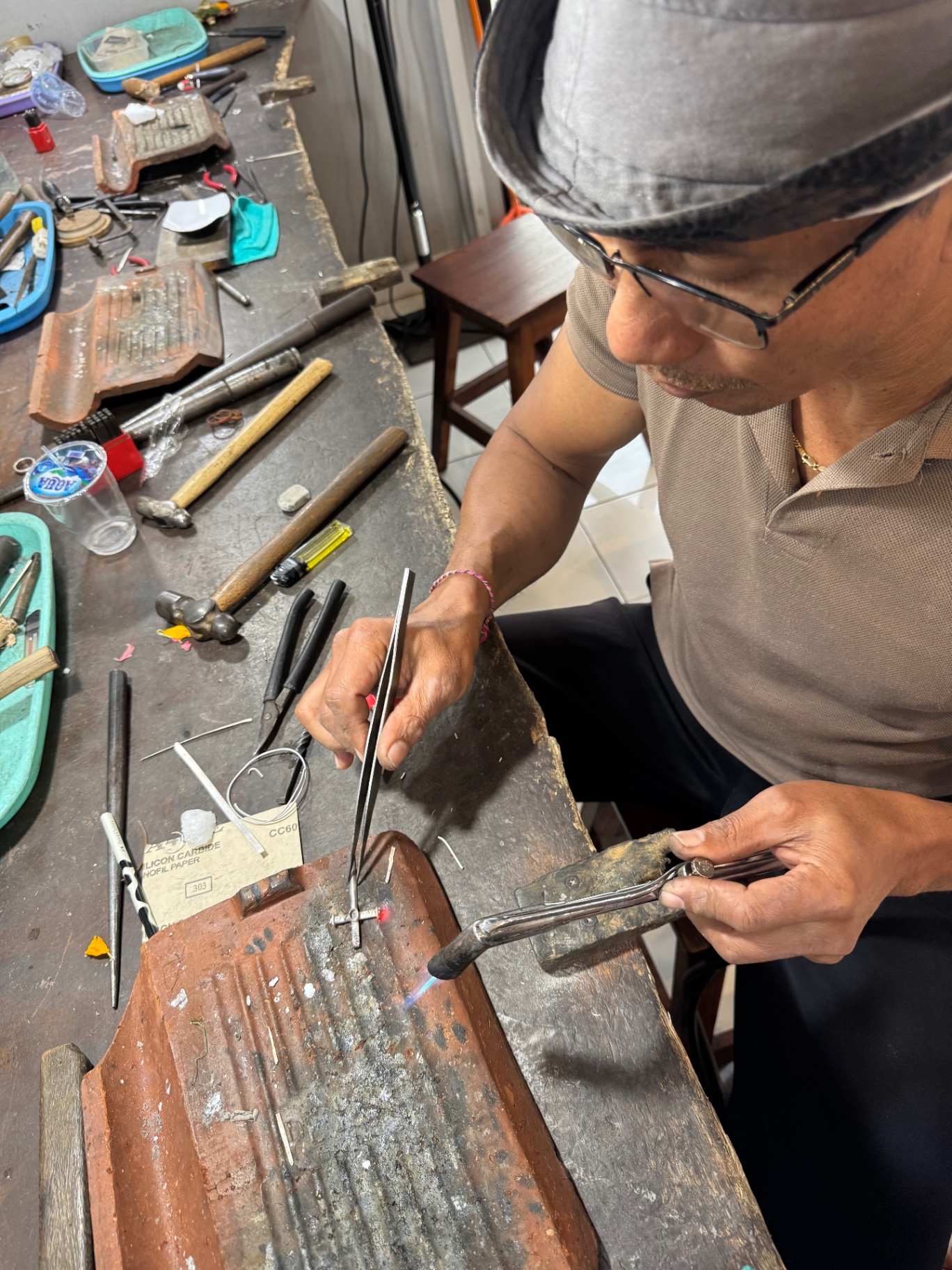 The silversmith shaping the cross with a torch at the workbench